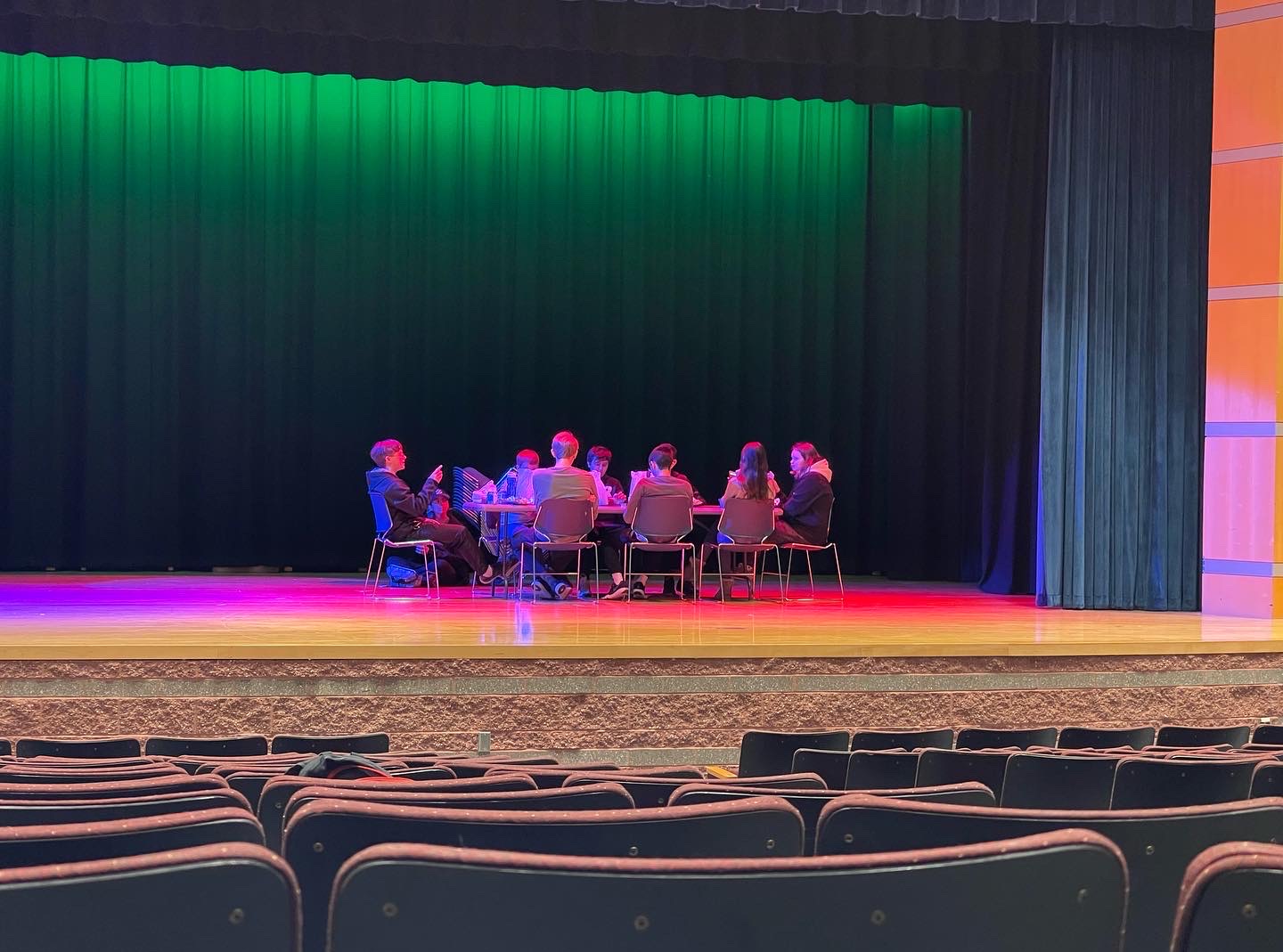 Students eating lunch together on the stage with colorful lighting during a break. 