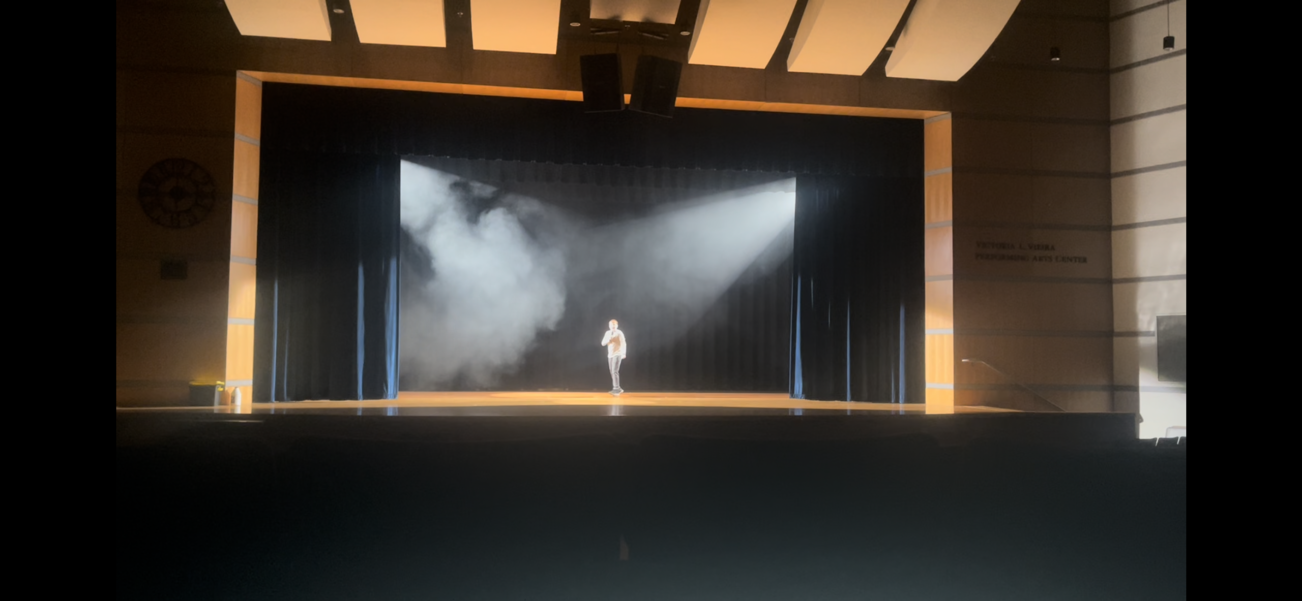 Student singing on the stage while lights and smoke fill the air.
