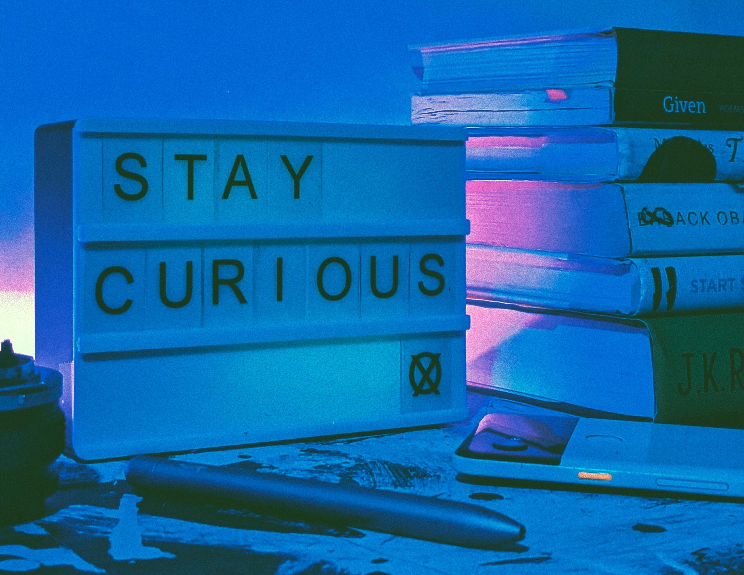A stack of books and a light up sign that says Stay Curious