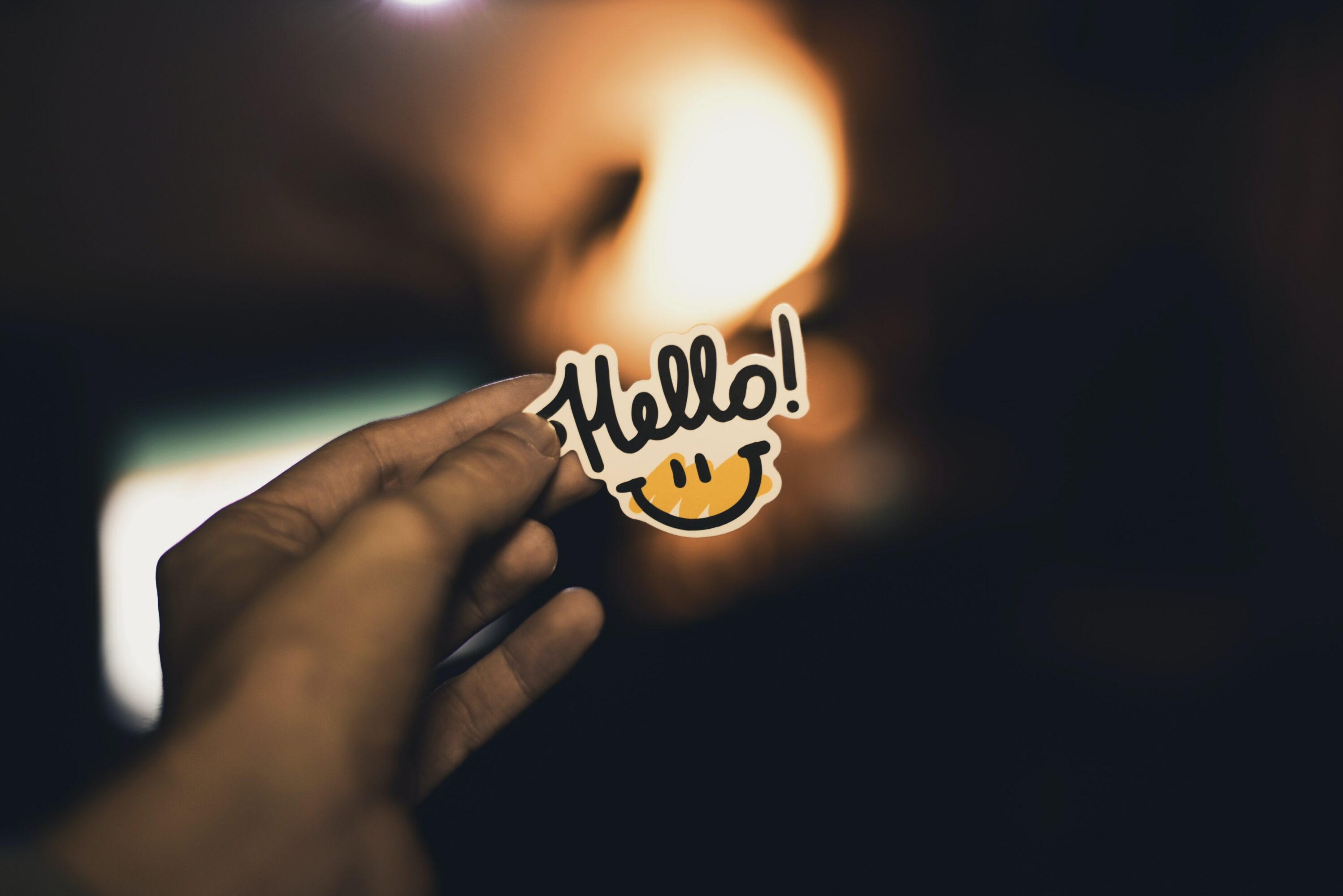 a hand holding a Hello! sticker with a smiley face.
