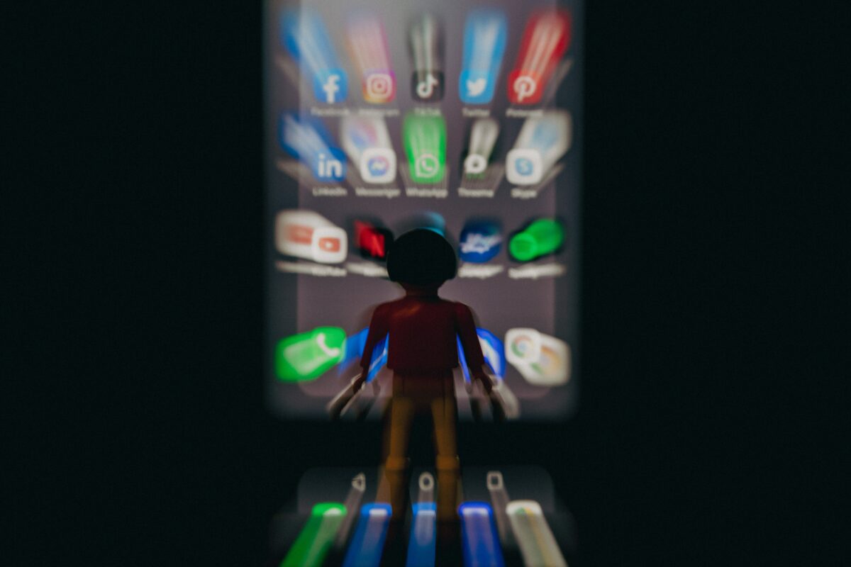 a blurry cartoon child standing in front of a blurry giant ipad with many social media icons on it.