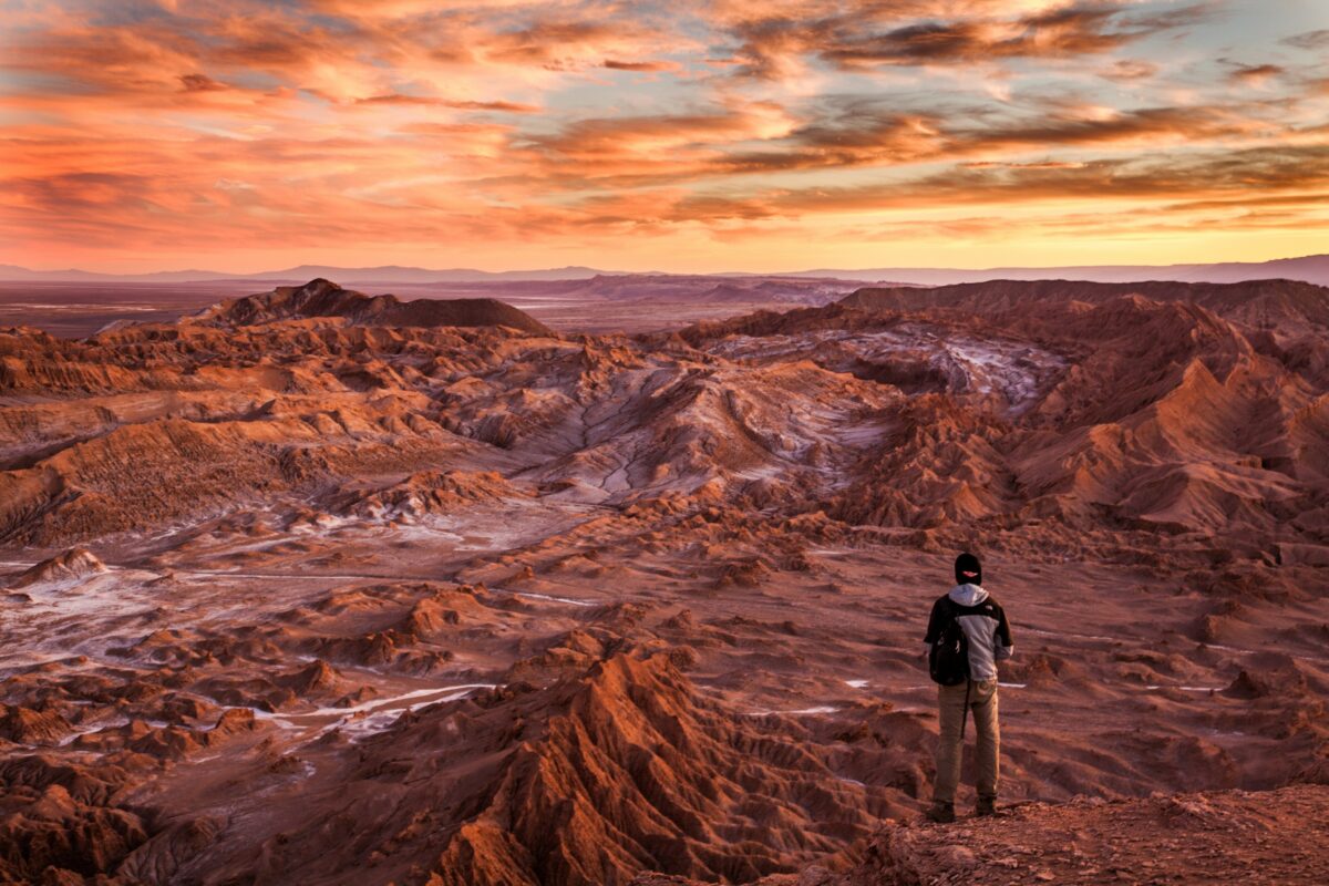 a mars-like landscape with a single person standing at the edge looking at it.