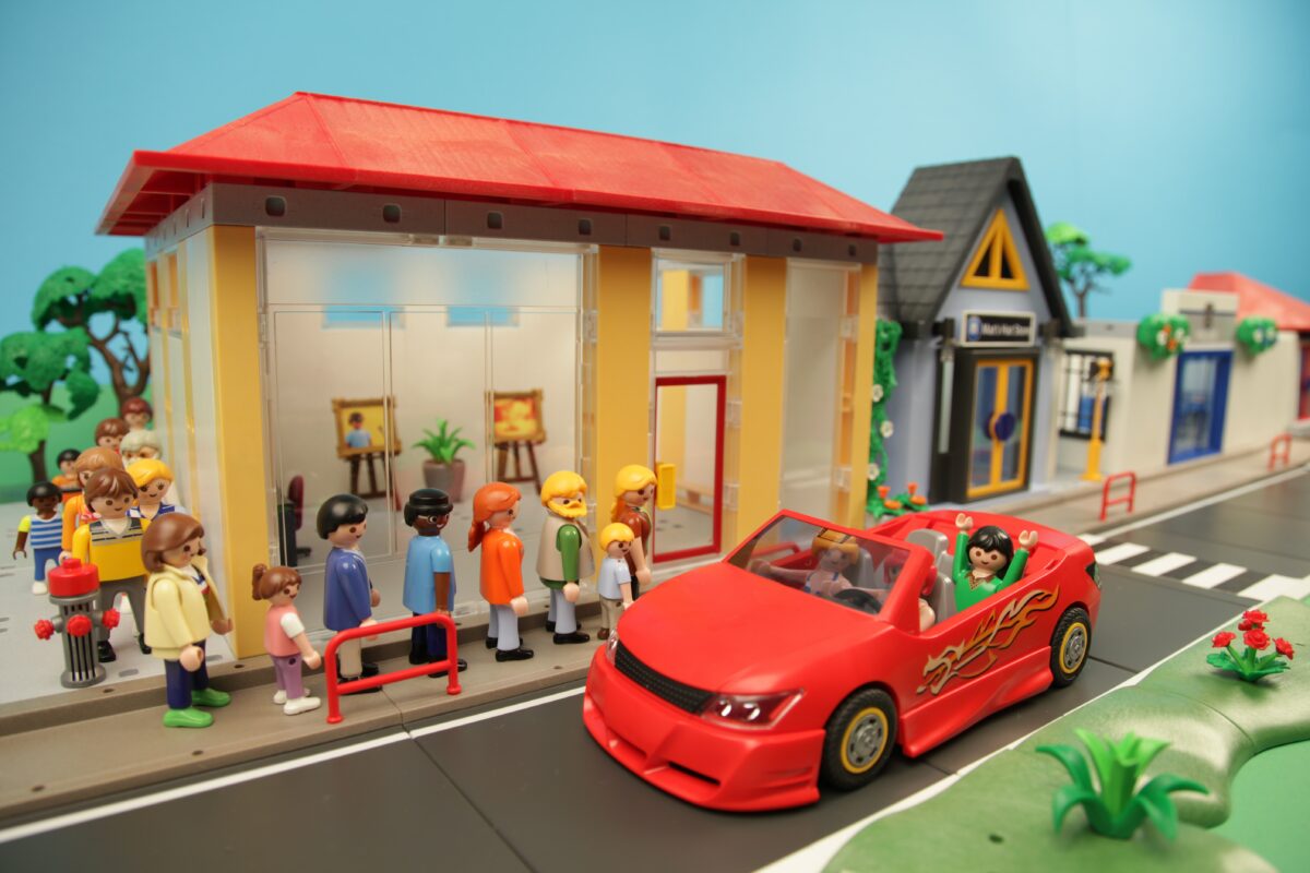 A PlaMobile town scene including some small people characters, a building and a red convertible car.