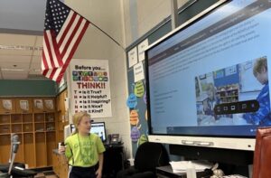 A young student presents to an audience in front of an interactive whiteboard.