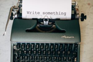 An antique typewriter with a piece of paper inside with the words "write something" typed on it.